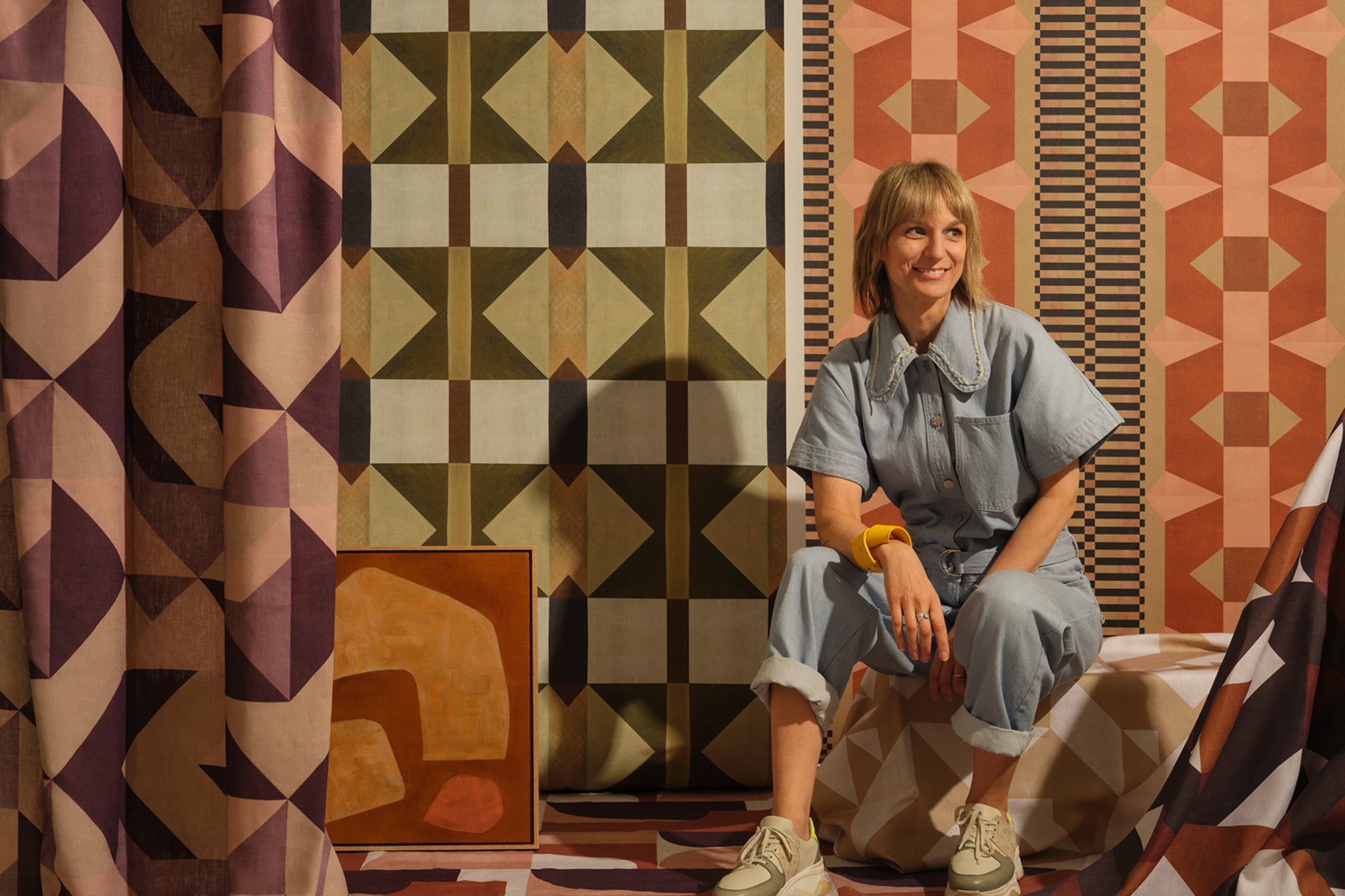 Portait of a blonde woman in a denim jumpsuit, against a colorful geometric background