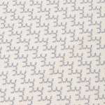 Detail of embroidered fabric in a linear geometric print in white and navy on a cream field.