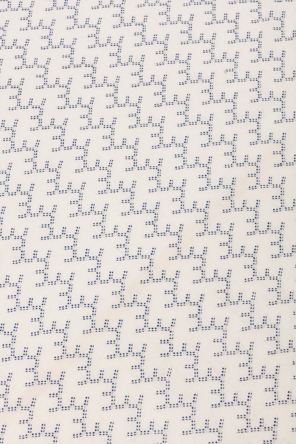 Detail of embroidered fabric in a linear geometric print in white and navy on a cream field.