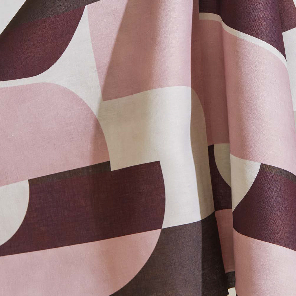 Draped fabric yardage in a curvilinear geometric print in pink and maroon on a white field.