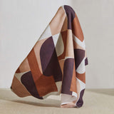 A large piece of draped fabric in a curvilinear geometric print in peach, purple and rust on a white field.