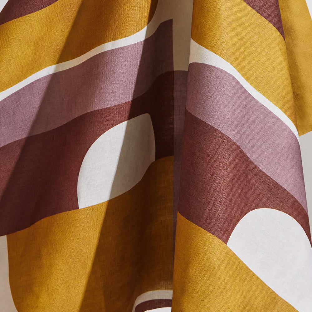 Draped fabric yardage in a curvilinear geometric print in purple, maroon and mustard on a white field.