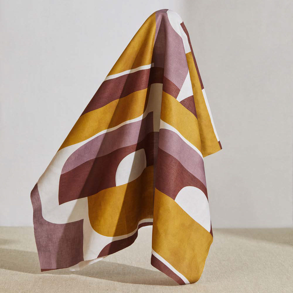 A large piece of draped fabric in a curvilinear geometric print in purple, maroon and mustard on a white field.