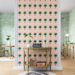 A maximalist living space with an accent wall papered in a repeating palm tree print in turquoise, brown, pink and white.