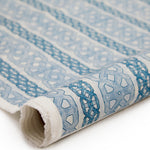 Partially unrolled fabric in a geometric stripe print in blue and navy on a mottled tan field.