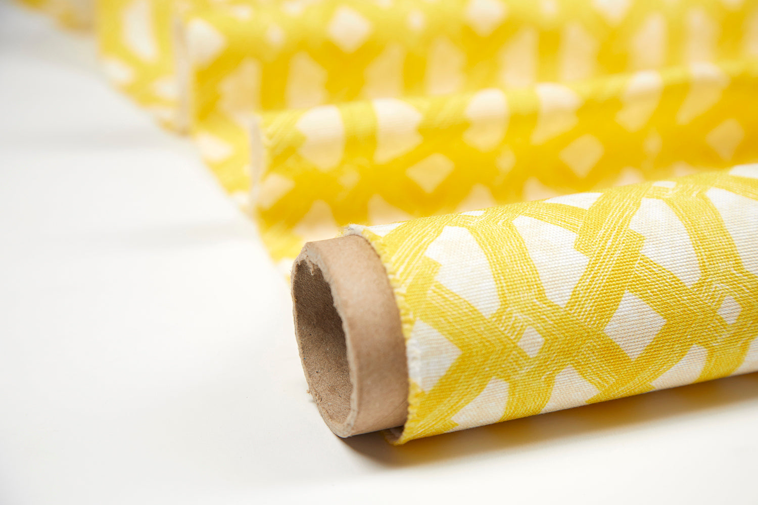 Partially unrolled fabric in an intricate lattice print in yellow on a cream field.