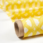 Partially unrolled fabric in an intricate lattice print in yellow on a cream field.