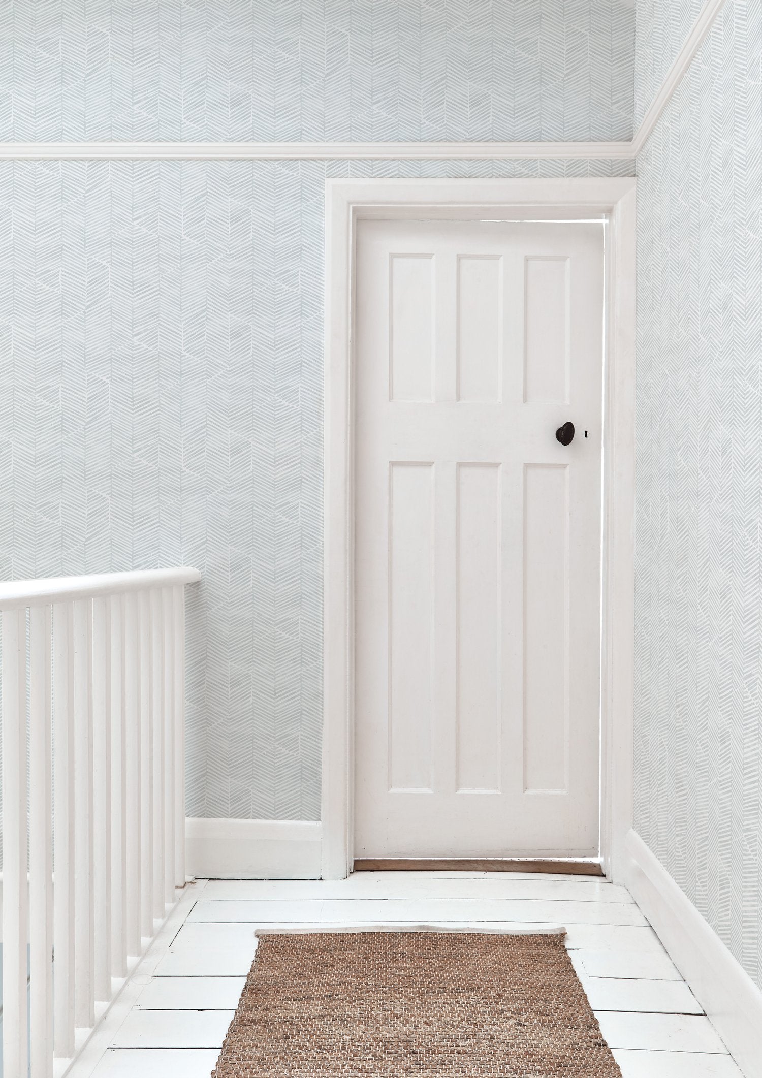 A door stands at the end of a hallway papered in a dense herringbone print in light gray on a white field.