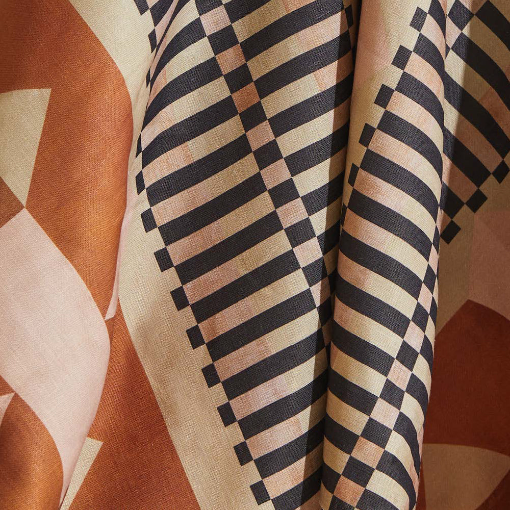 Draped fabric yardage in a dense geometric print in shades of pink, orange and brown on a cream field.