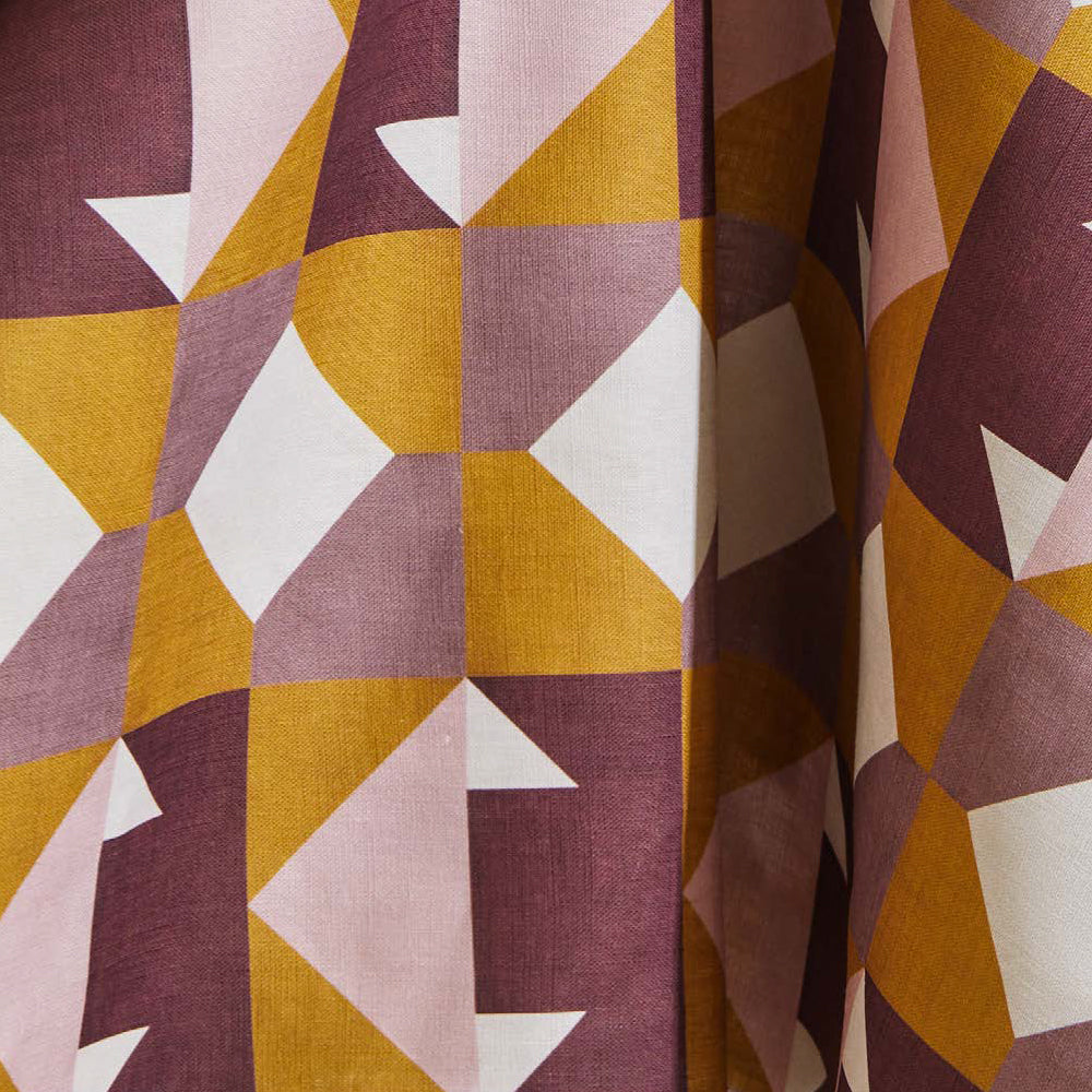 Draped fabric yardage in a geometric grid print in mustard, pink and purple on a white field.
