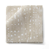Stacked fabric swatches in a painterly small-scale dashed dot print in white on a soft taupe watercolor field.