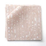 Stacked fabric swatches in a painterly small-scale dashed dot print in white on a soft pink watercolor field.