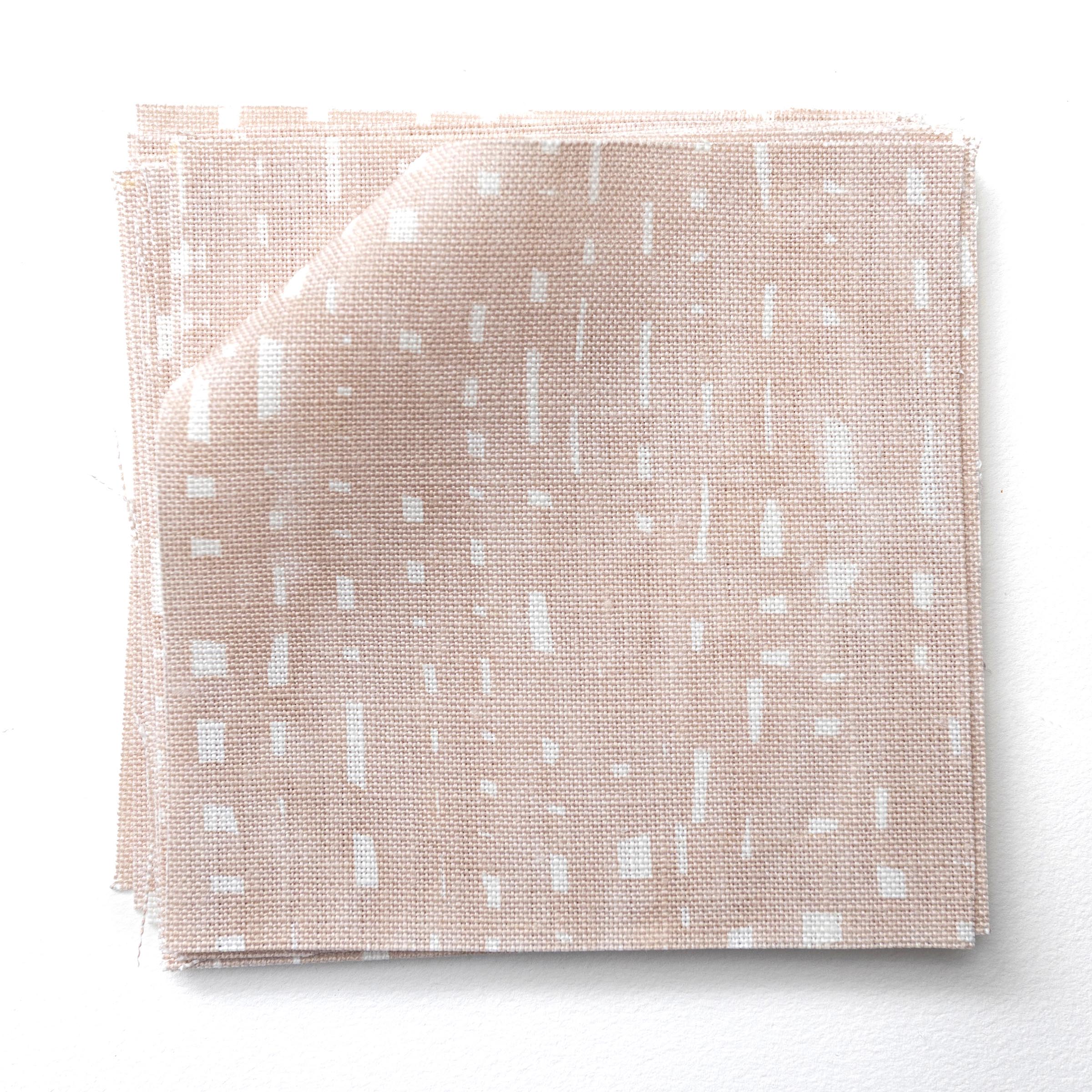 Stacked fabric swatches in a painterly small-scale dashed dot print in white on a soft pink watercolor field.