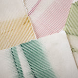 Pile of wallpaper swatches with dimensional combed patterns in green, gold and pink colorways on cream fields.