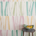 A stool stands in front of a wall covered in an irregular striped wallpaper in shades of teal, pink, green and yellow.