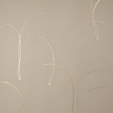 Detail of a wallpaper in an elongated paint splatter pattern in metallic gold on a cream field.