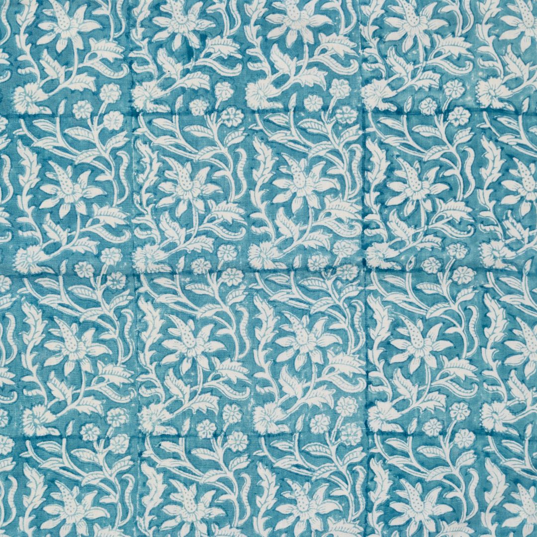 Detail of fabric in a floral block print in white on a turquoise field.