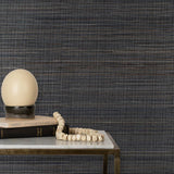 End table with books and a globe lamp in front of a wall papered in textured grasscloth in shades of grey, brown and black.