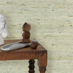 End table with marble and wood scupltures in front of a wall papered in textured pastel arrowroot grasscloth.