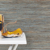 End table with a vase and sculptures in front of a wall papered in jute grasscloth in blue and brown.