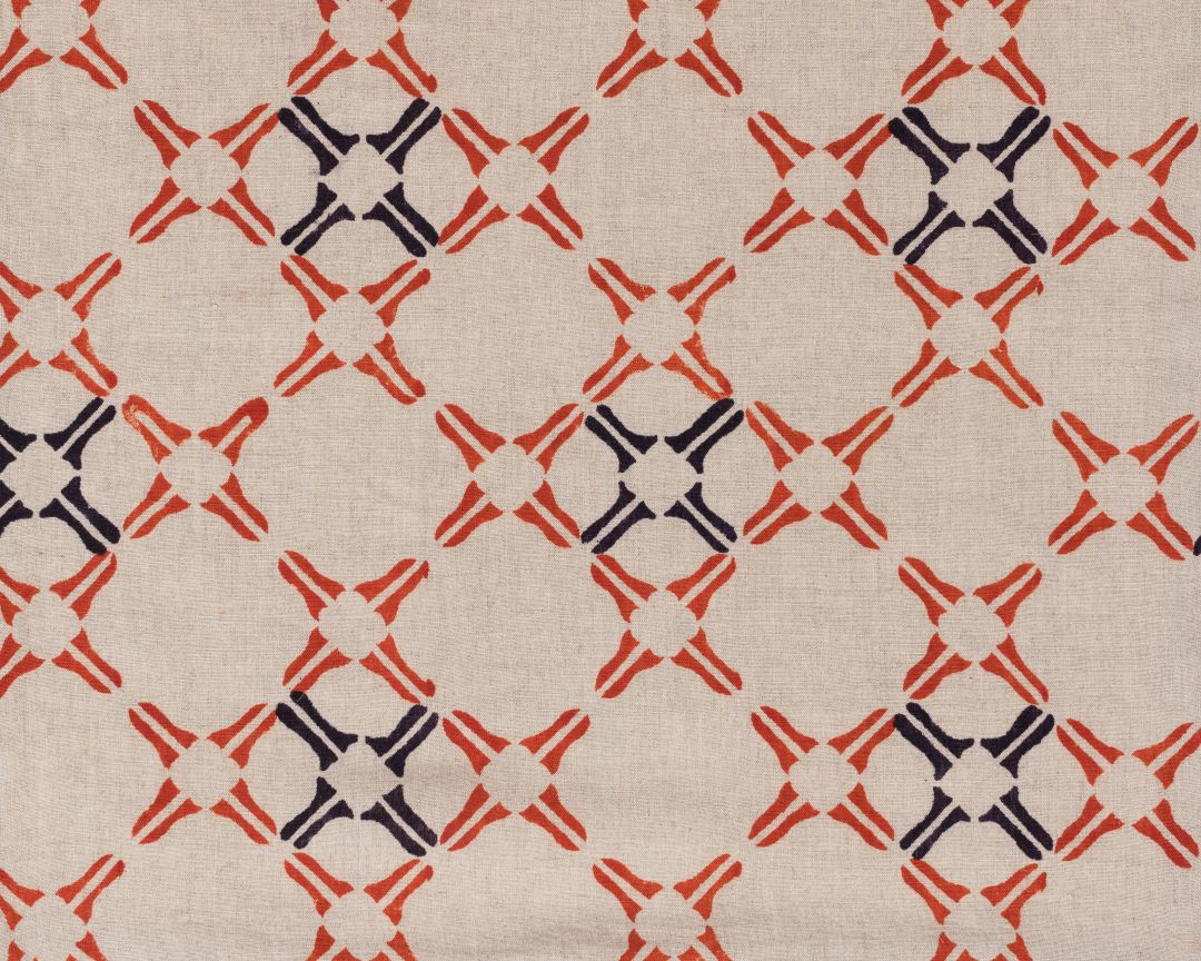 Detail of fabric in a geometric lattice print in orange and navy on a tan field.