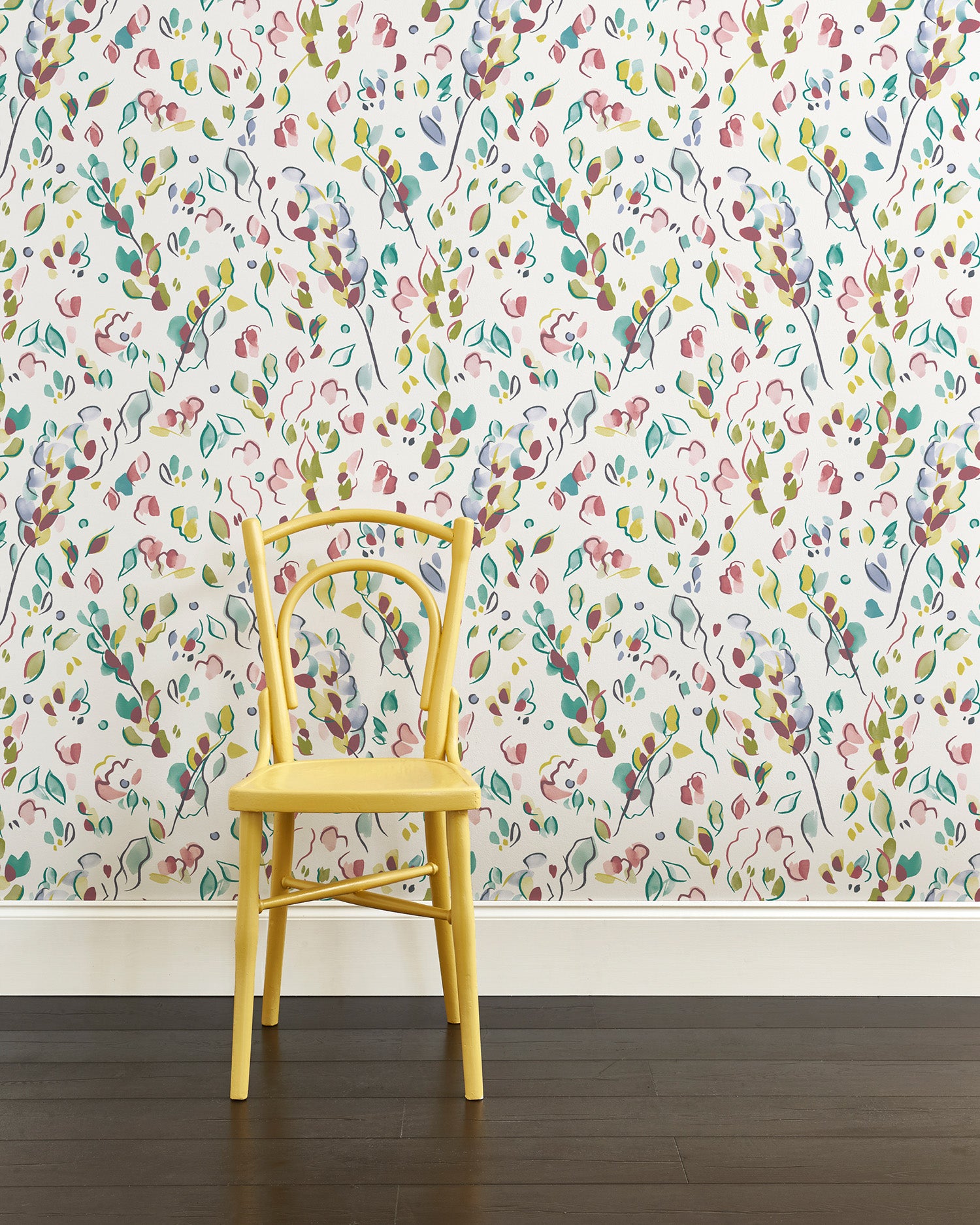 A yellow chair stands in front of a wall papered in a painterly leaf print in purple, blue, green and white.