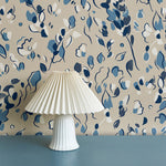 Modernist lamp in front of a wall papered in a painterly leaf print in shades of blue, white and tan.