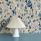 Modernist lamp in front of a wall papered in a painterly leaf print in shades of blue, white and tan.