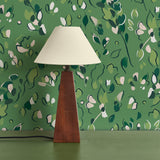 Modernist lamp in front of a wall papered in a painterly leaf print in shades of green.