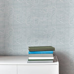 An end table with a stack of books stands in front of a wall papered in a dense herringbone print in light blue and white.
