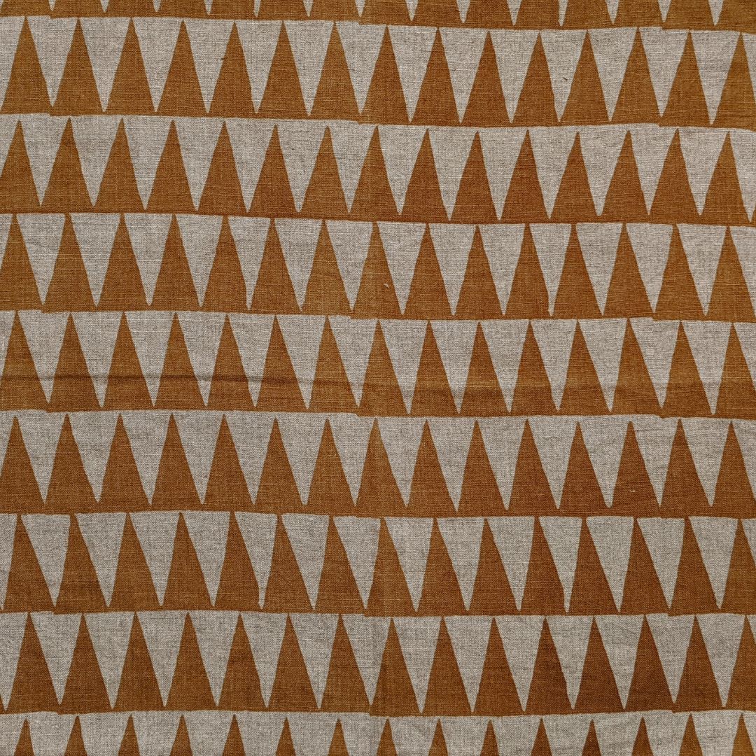 Detail of fabric in a repeating triangle print in burnt orange on a tan field.