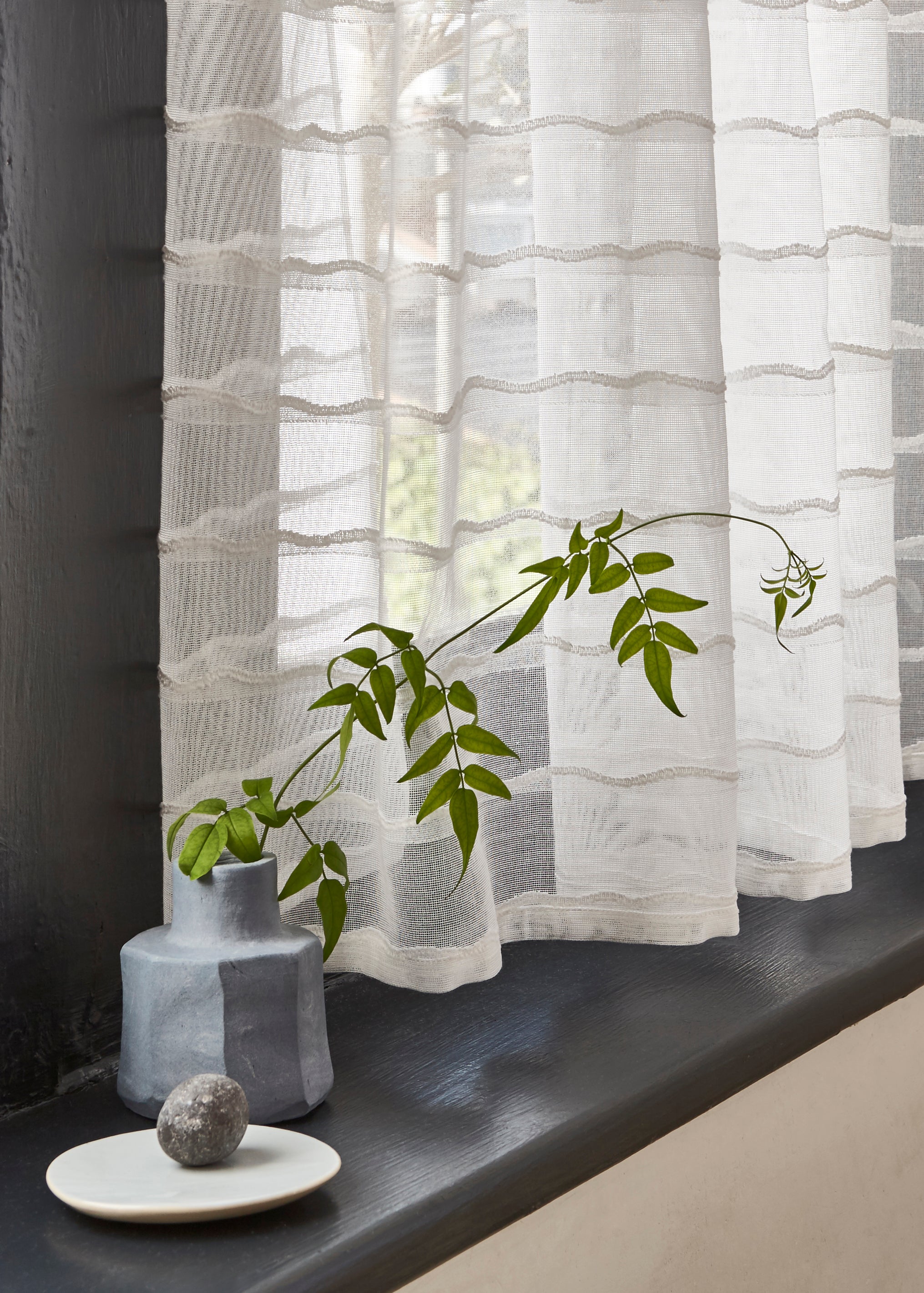 Windowsill with a vase and wildflower with a sheer fabric curtain in a wavy stripe pattern in ivory.