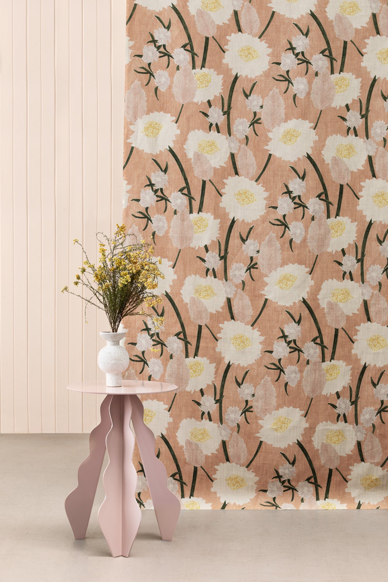 A mauve end table stands in front of a fabric curtain in a playful floral print in pink, white, yellow and green.