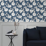 A couch and end table stand in front of a wall papered in a playful floral print in white, gray and navy.