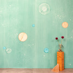 A table with knick knacks stands in front of a wall papered in a paint splatter print in pastels on a green field.