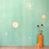 A table with knick knacks stands in front of a wall papered in a paint splatter print in pastels on a green field.