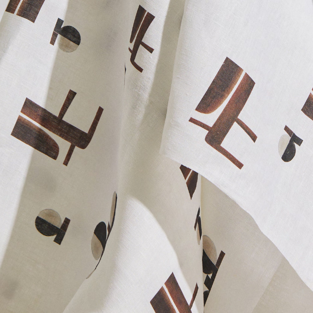 Draped fabric yardage in an abstract geometric print in brown and tan on a white field.