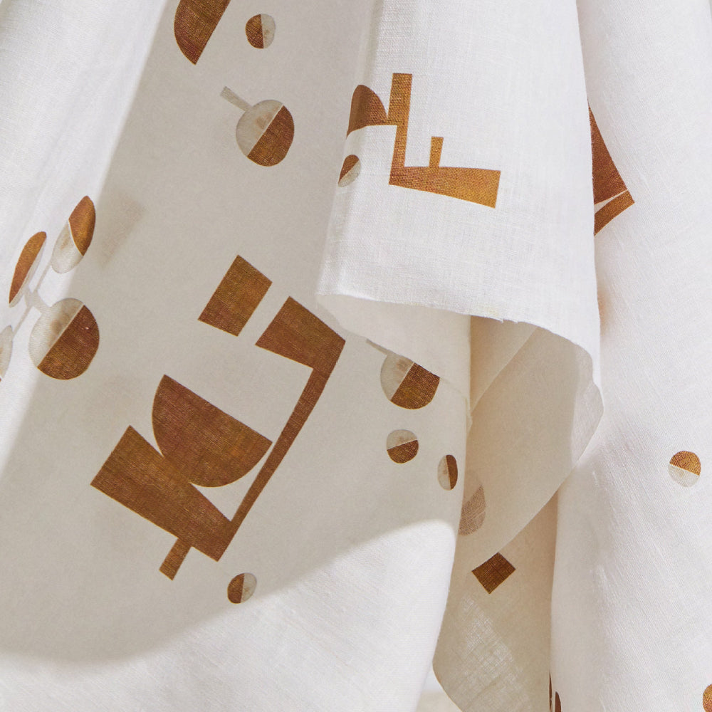 Draped fabric yardage in an abstract geometric print in mustard and cream on a white field.