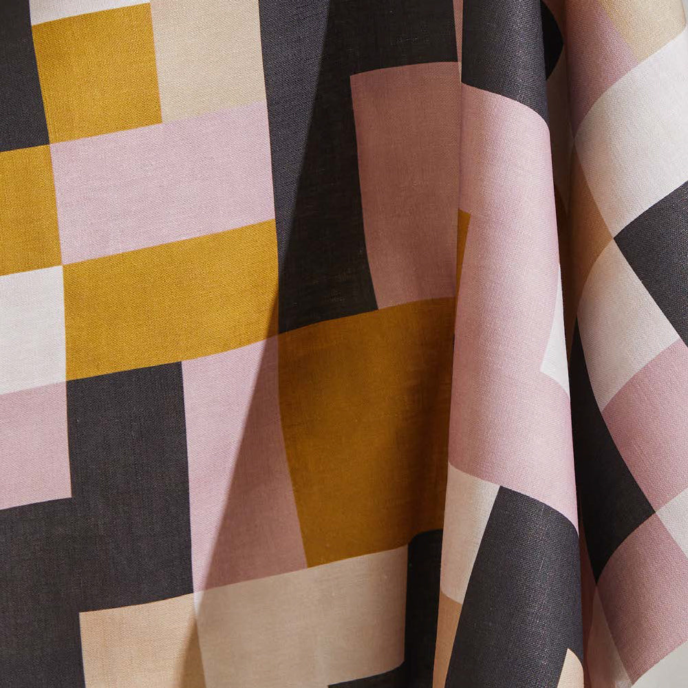 Draped fabric yardage in an interlocking square pattern in shades of pink, purple, mustard and cream.