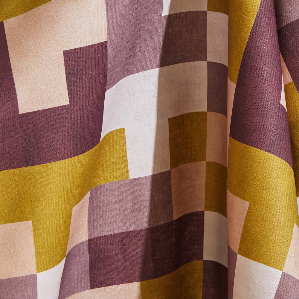 Draped fabric yardage in an interlocking square pattern in shades of purple, mustard and cream.