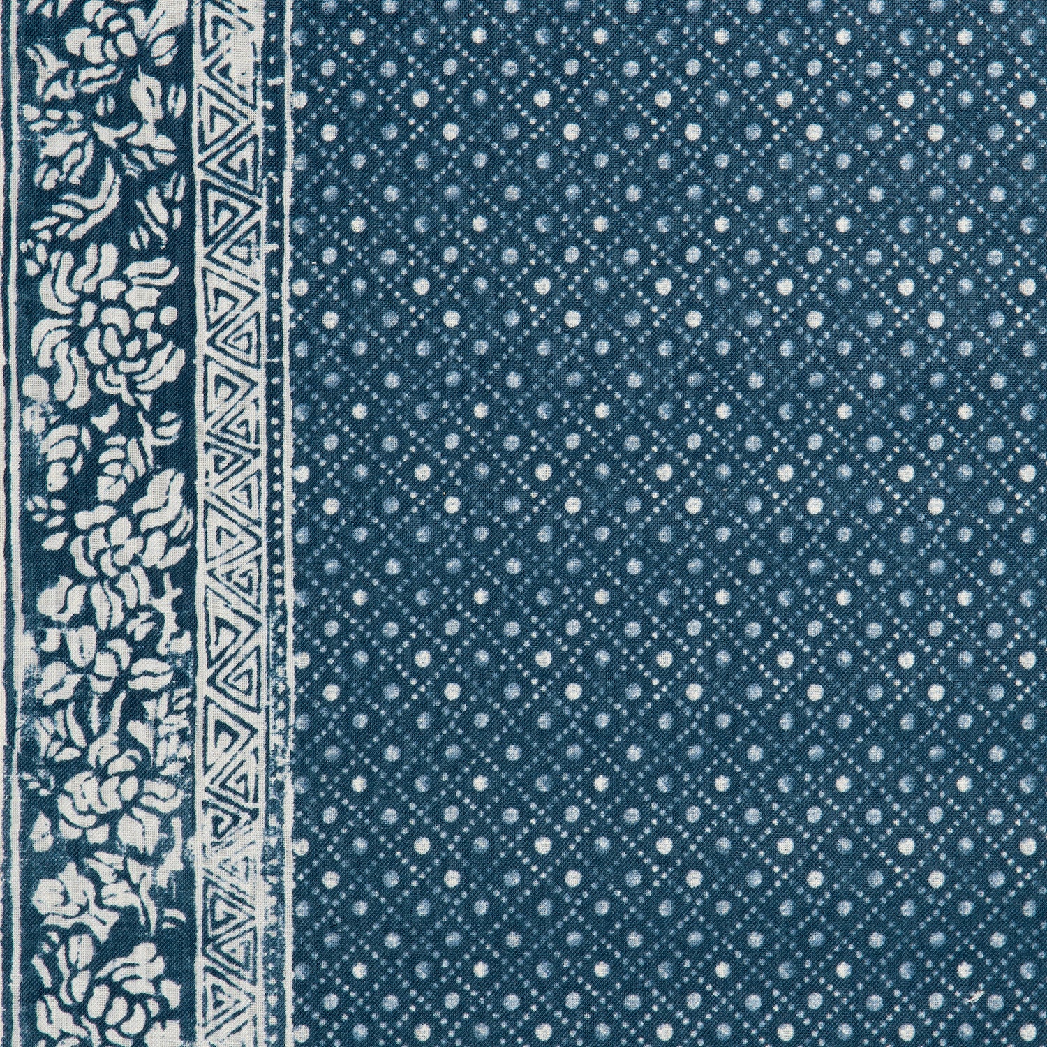 Detail of a linen fabric in a gridded dot pattern with a floral border in white on an indigo field.