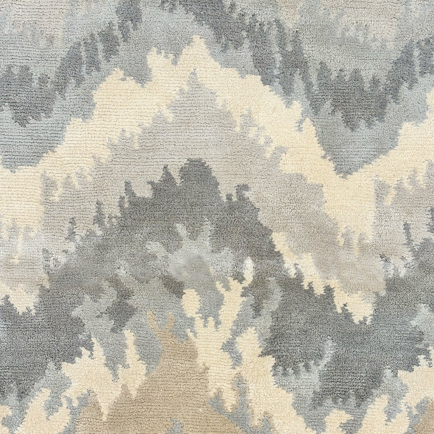 Detail of a handknotted rug in a painterly ikat chevron pattern in soft shades of grey. 