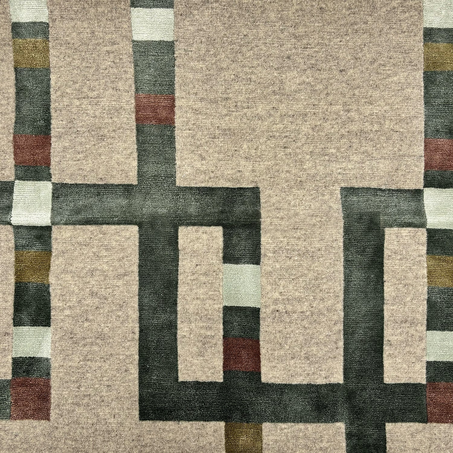 Detail of a handknotted rug with a minimlist geometric stripe pattern in shades of green agaist a brown field.