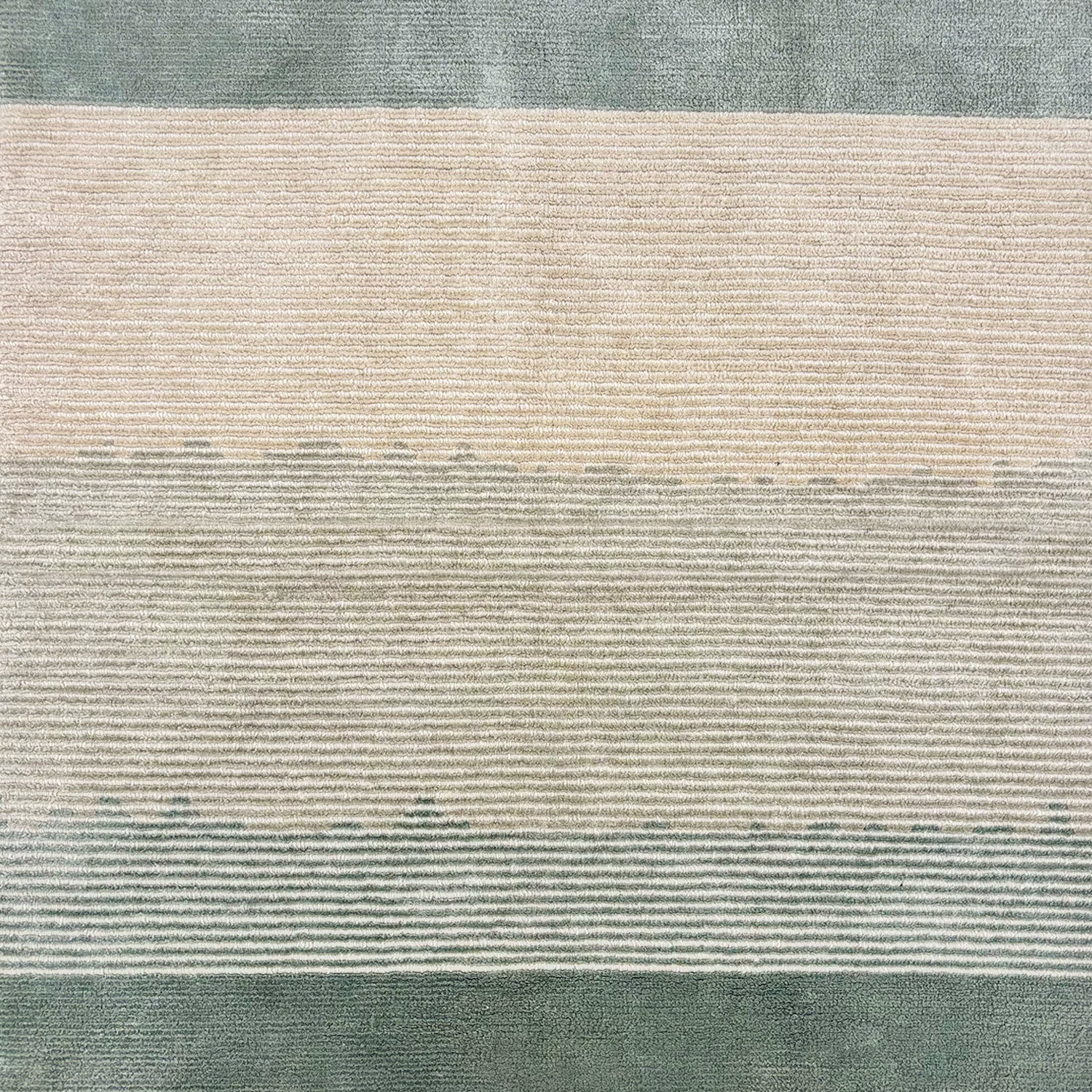 Detail of a handknotted rug with a subtle ombré effect from cream to sage green, with sage green borders