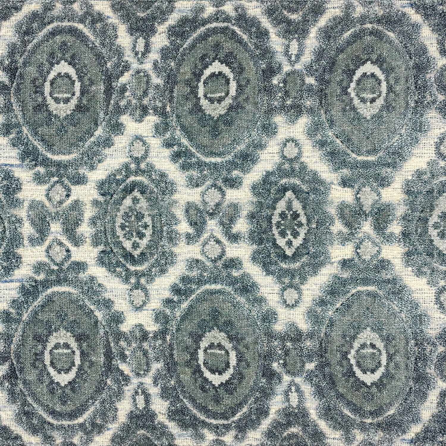 Detail of a handknotted rug with a floral medallion pattern in shades of acqua and grey. 