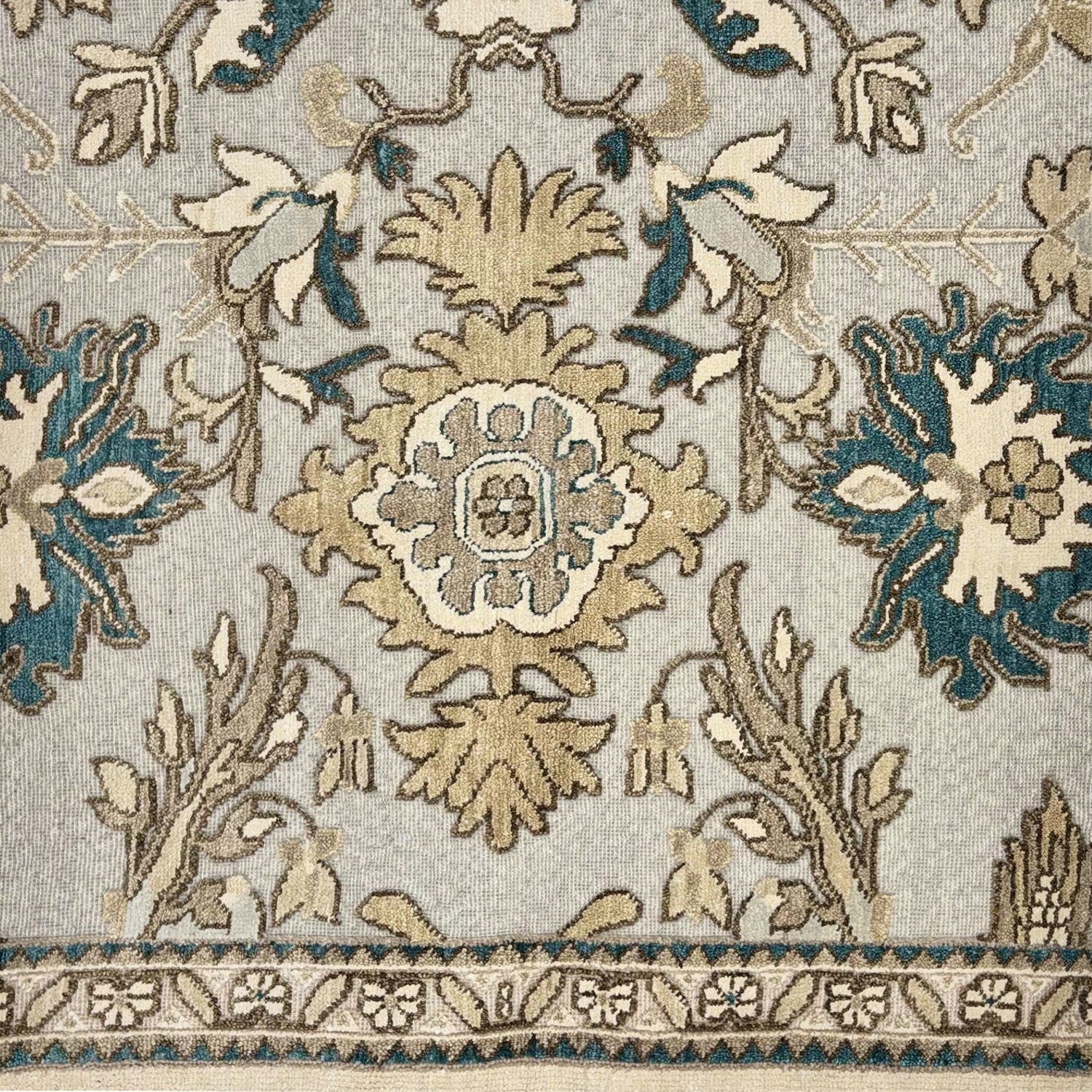 Detail of a rug with an old world inspired pattern in cream, grey and teal.