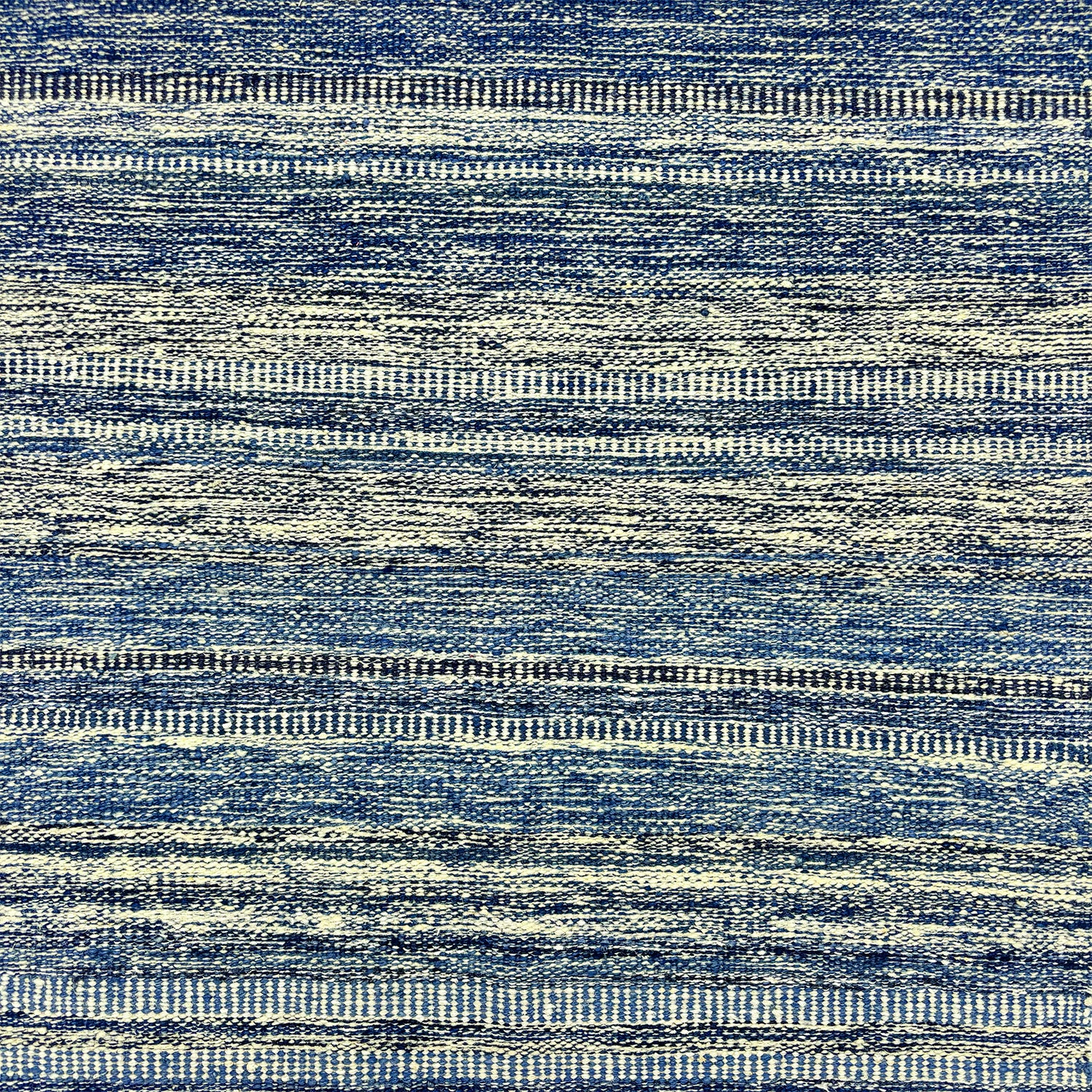 Detail of a wool rug with a textural strié stripe pattern in indigo and cream