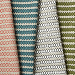 Row of overlapping folded fabrics, each in a honeycomb grid pattern in different pink, blue and green colorways on cream fields.
