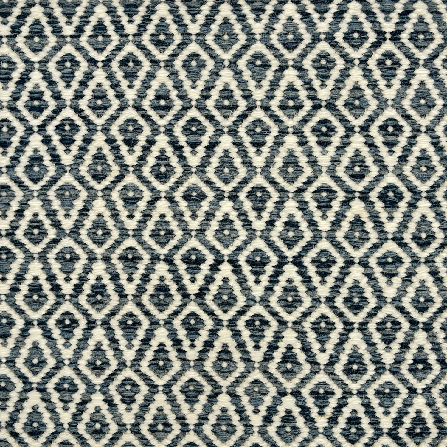 Detail of a handowven rug in an diamond like pattern in white and shades of blue.