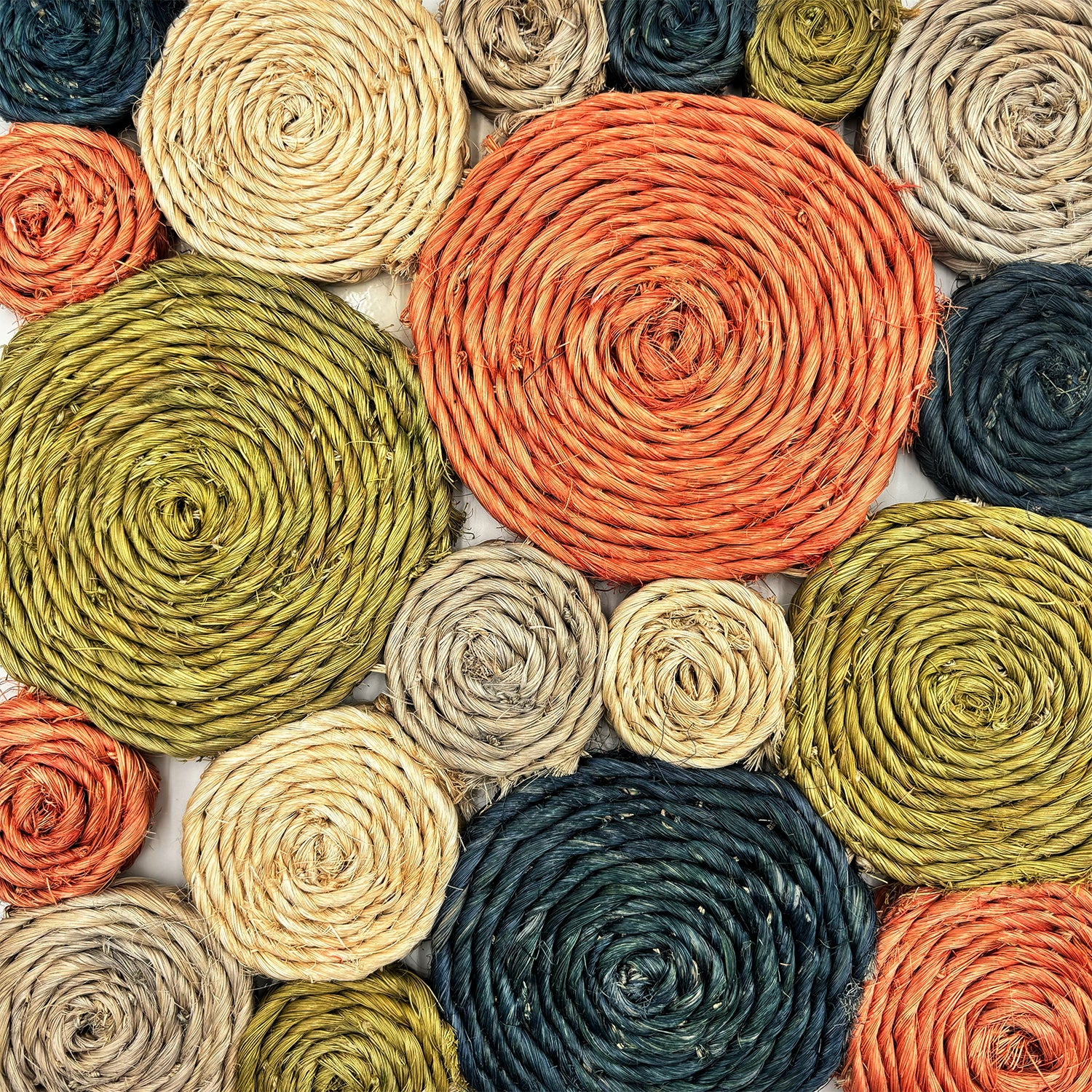 Detail of a handwoven abaca rug made of circles in varying sizes, in blue, tan, and orange. 
